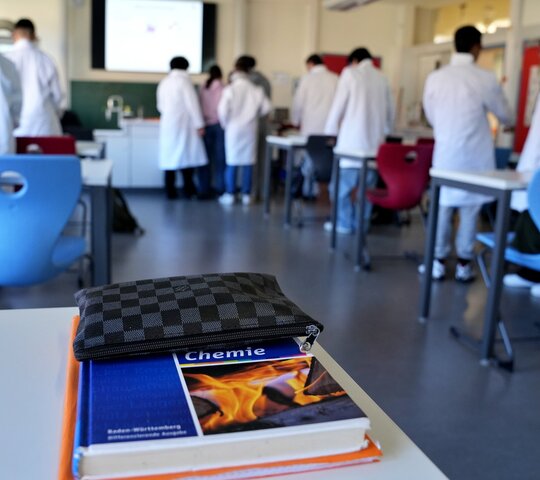 Das Foto zeigt eine Klasse beim Chemieunterricht, im Vordergrund ist ein Chemiebuch zu sehen