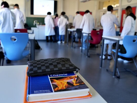Das Foto zeigt eine Klasse beim Chemieunterricht, im Vordergrund ist ein Chemiebuch zu sehen