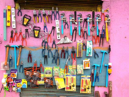 An einer leuchtend pinkfarbenen Wand hängt diverses Werkzeug, Zangen, Hammer, Wasserwaagen etc.