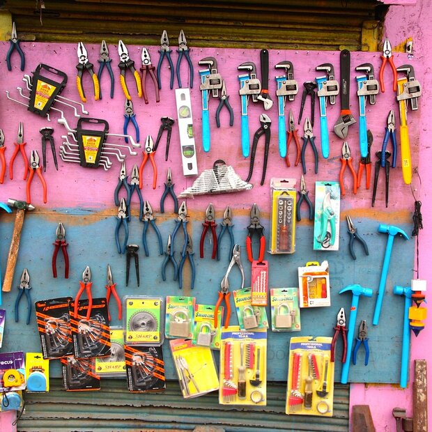 An einer leuchtend pinkfarbenen Wand hängt diverses Werkzeug, Zangen, Hammer, Wasserwaagen etc.