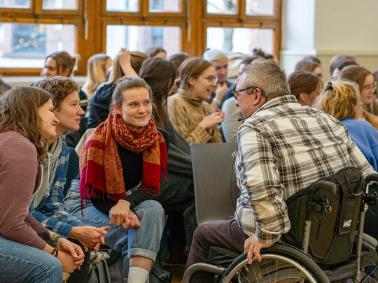 Studierende tauschen sich mit Bildungsfachkräften des AW-ZIB aus; im Vordergrund ein Herr im Rollstuhl, der sich mit Studentinnen unterhält.