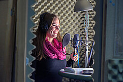 Das Symbolbild zeigt eine junge Frau im Tonstudio. Sie spricht lächelnd in ein Mikrofone. Copyright Pädagogische Hochschule Heidelberg