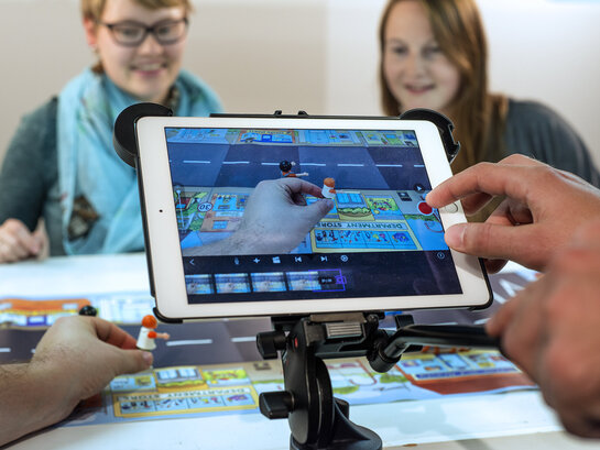 Zwei Studentinnen im Hintergrund, im Vodergrund wird ein iPad bedient.