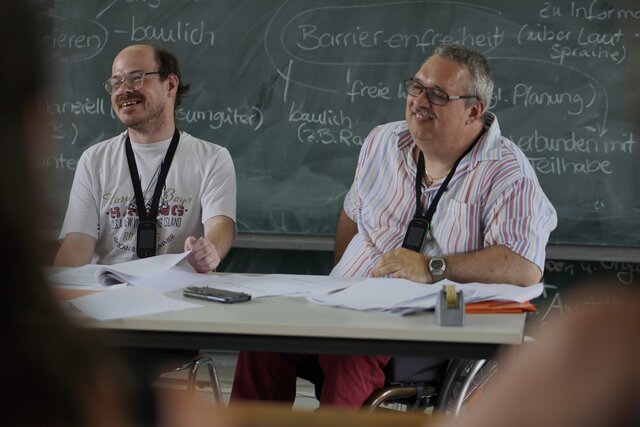 Das Bild zeigt die Bildungsfachkräfte Thilo Krahnke und Helmuth Pflantzer während eines Bildungsangebots. Sie sitzen vor einer Tafel in einem Hörsaal der PH Heidelberg.