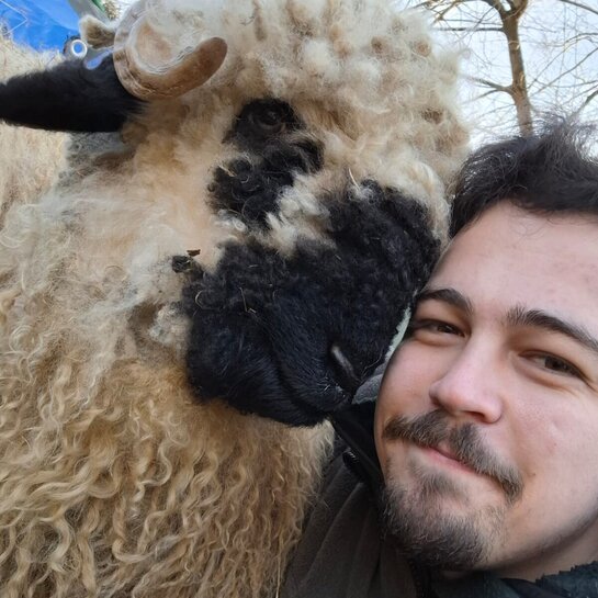 Luca lächelt zusammen mit einem sehr flauschigen Schaf in die Kamera.