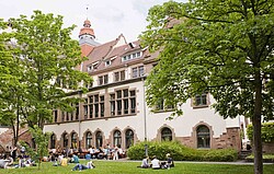 Das Foto zeigt den Innenhof des Altbaues. Auf der Wiese liegen und sitzen einige Studierende.