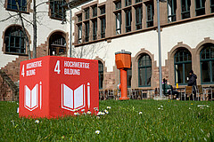 Eine Würfel auf dem das SDG4 Hochwertige Bildung abgebildet ist, steht im Innenhof des Altbaus.