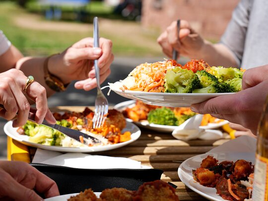 Das Foto zeigt einen Mittagstisch mit vollen Tellern und die Hände der essenden Menschen