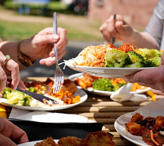 Das Foto zeigt einen Mittagstisch mit vollen Tellern und die Hände der essenden Menschen