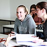 Das Bild zeigt mehrere Studierende, die sich an einem Tisch gegenübersitzen und miteinander reden.