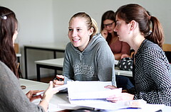 Das Bild zeigt mehrere Studierende, die sich an einem Tisch gegenübersitzen und miteinander reden.
