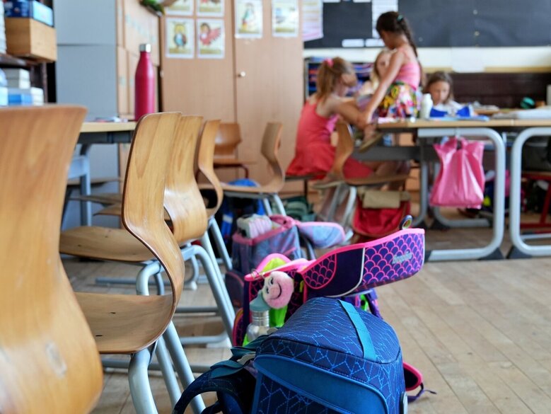 Zu sehen sind Schulranzen und Kinder im Hintergrund in einem Klassenzimmer
