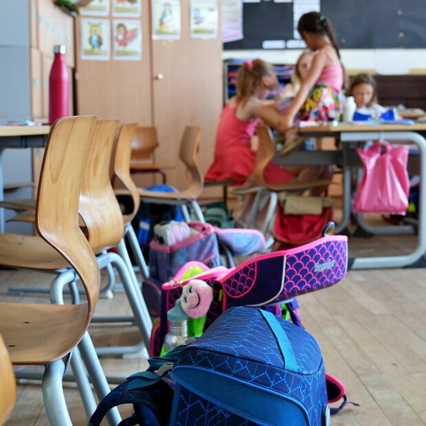Zu sehen sind Schulranzen und Kinder im Hintergrund in einem Klassenzimmer