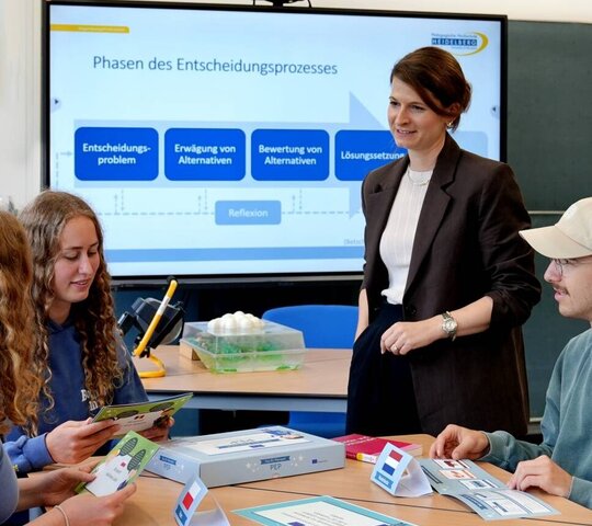 Zu sehen ist eine Dozierende und Studierende vor einer Tafel.