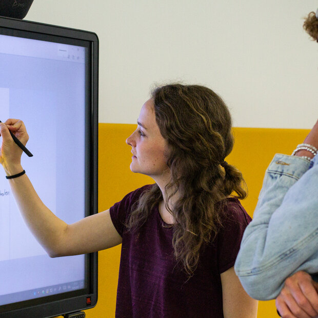 Eine Studentin markiert an einem Smartboard eine Grafik zur Erderwärmung. Neben ihr ein Kommilitone.