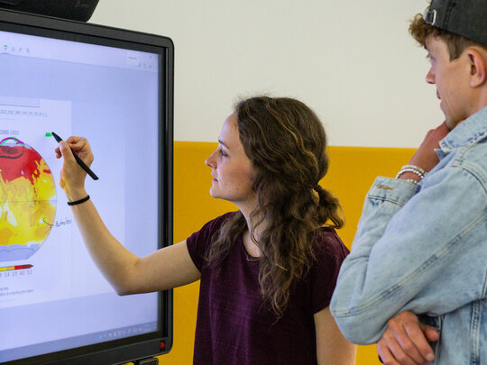Eine Studentin markiert an einem Smartboard eine Grafik zur Erderwärmung. Neben ihr ein Kommilitone.