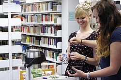  zwei Studierende vor vielen Bücherregalen.