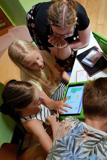 Lehrer Kinder beugen sich über einen Tisch mit Tablets in der Hand. 