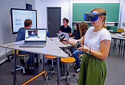  Frau mit einer VR-Brille und zwei Controllern in der Hand. 