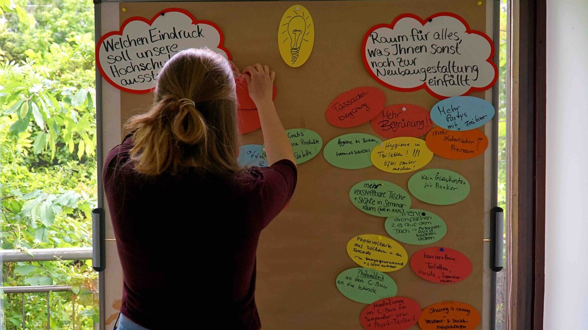 eine Studentin steht vor einer Pinnwand mit bunten Zetteln 