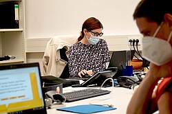 zwei Personen an jeweils einem Laptop in einem Büro arbeiten. 