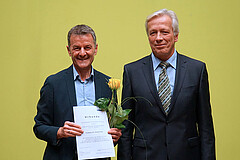 Markus Lang und Karl-Heinz Dammer. Lang hat die Lehrpreis-Urkunde und eine gelbe Rose in der Hand. Beide schauen freundlich in die Kamera.