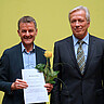 Markus Lang und Karl-Heinz Dammer. Lang hat die Lehrpreis-Urkunde und eine gelbe Rose in der Hand. Beide schauen freundlich in die Kamera.