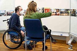 Das Bild zeigt zwei Personen, eine davon sitzt im Rollstuhl. Beide schauen sich ein Bildgalerie an. Copyright Pädagogische Hochschule Heidelberg