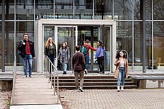 Das Bild zeigt verschiedene Hochschulangehörige vor dem Hörsaalgebäude.