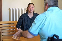 Das Bild zeigt primär Noemi Heister; sie lächelt Helmuth Pflantzer an. Diesen sieht man von hinten; er redet deutlich mit den Händen. Die beiden sitzen im Altbau der Hochschule.