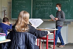 Das Symbolbild ein Klassenzimmer. Ein Lehrer steht vor einer Tafel und hält ein Arbeitsblatt in der Hand. Copyright Pädagogische Hochschule Heidelberg