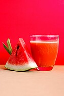Abgebildet sind ein Stück Wassermelone und ein Glas mit Melonensaft