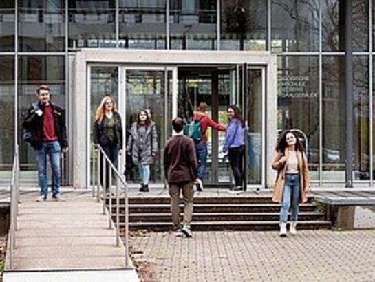 Das Bild zeigt Studierende, die aus einem Hochschulgebäude raus und reingehen. 
