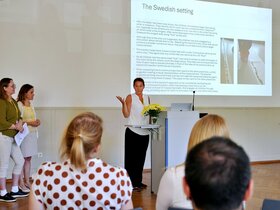 Zu sehen ist eine Wissenschaftlerin beim Erklären vor dem Auditorium