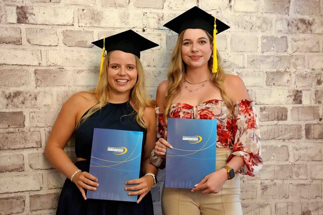 Zu sehen sind zwei Alumnae mit Graduierungshut in der Fotobox, wie sie ihre PHHD-Mappen hochhalten.