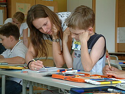 Lehrende die einem Jungen bei einer Aufgabe in der Schule hilft.