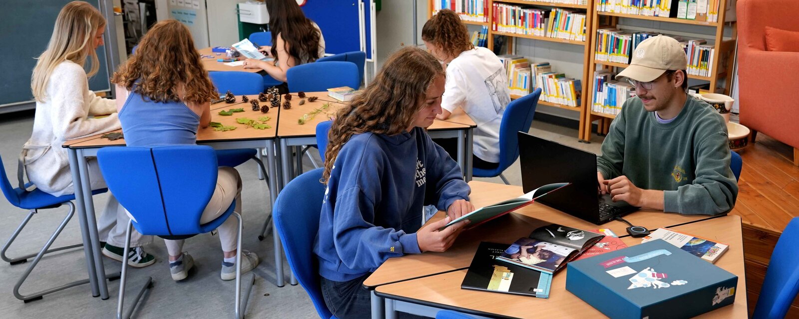 Zwei Studentinnen sitzen an einem Tisch und interagieren mit einer Handpuppe.