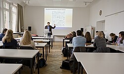 Das Bild zeigt einen Seminarraum, in dem mehrerer Studierende sitzen. An dem Whiteboard zeigt ein Dozierender auf die Schrift. Copyright Pädagogische Hochschule Heidelberg