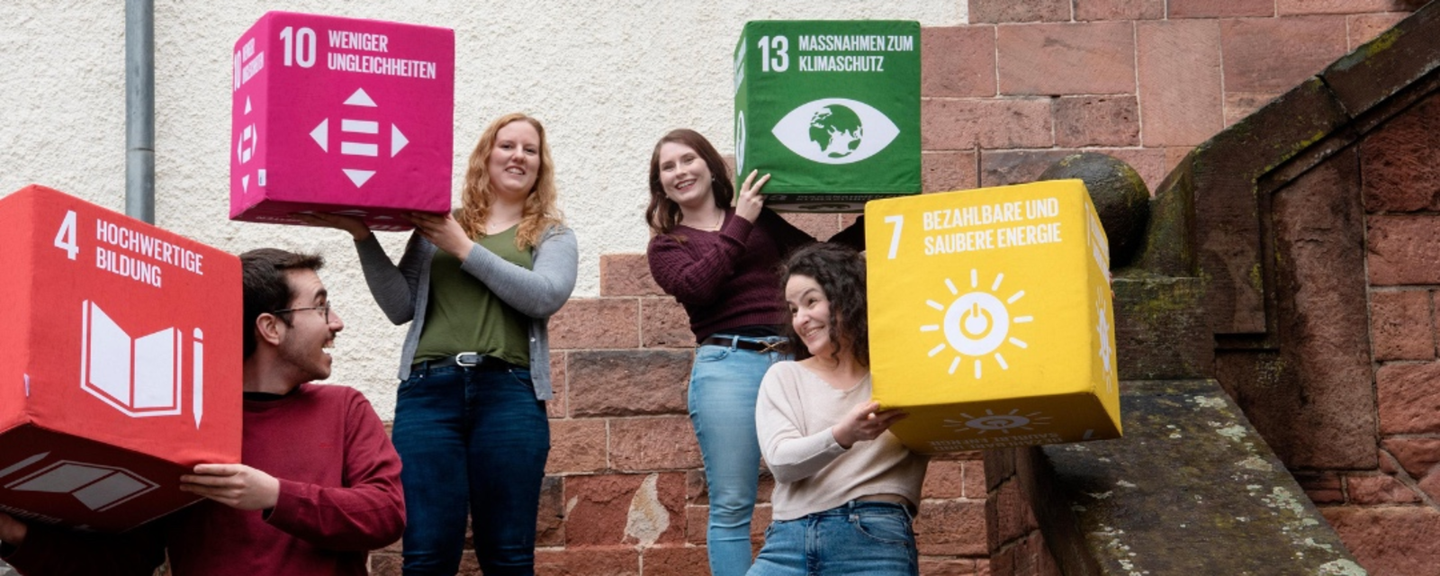 Studierende des Digitale Bildung für nachhaltige Entwicklung halten große bunte Würfel mit den SDGs hoch.