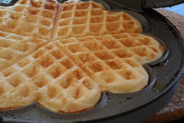 Eine fertige Waffel liegt in einem Kleeblattförmigen Waffeleisen.