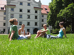 Auf dem Symbolbild sieht man Studierende. Sie sitzen im Gras und unterhalten sich. Im Hintergrund sieht man die PH Weingarten. 