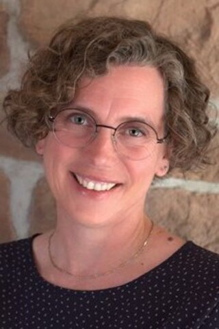 Zu sehen ist ein Portraitfoto von Ulrike Fesller vor einer gemauerten Wand.