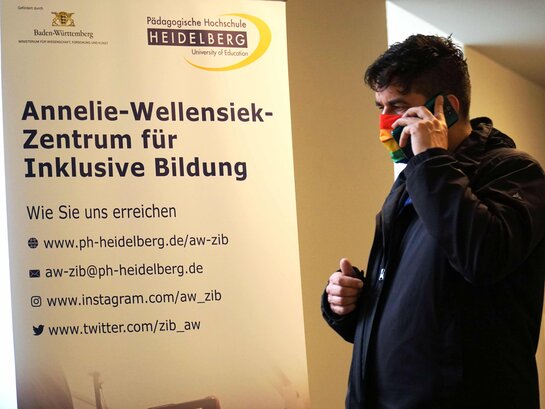 Das Bild zeigt Herrn Dr. Klemens Ketelhut beim telefonieren vor einem Informationsplakat der AW-ZIB.