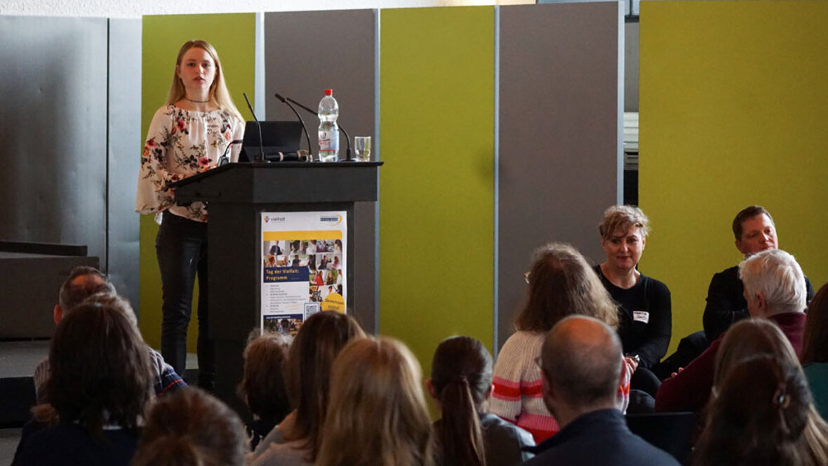 Eine Studentin am Rednerpult in der Festhalle. Das Publikum sieht man unscharf von hinten.