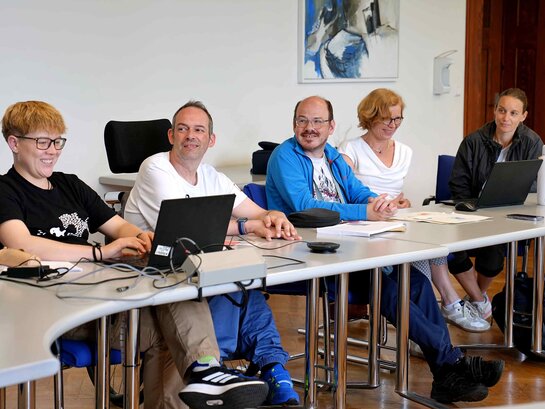 Das Foto zeigt eine Situation im Forschungsplenum: Eine Studentin, zwei Bildungsfachkräfte und zwei zur Promotion abgeordnete Lehrerinnen sitzen im Senatssaal an einem Tisch. Die Studentin hat einen Laptop vor sich.