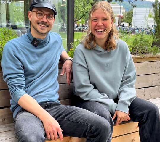 Der Tutor und die Tutorin der Sprecherziehung der Pädagogischen Hochschule Heidelberg sitzen auf einer Bank und strahlen in die Kamera.