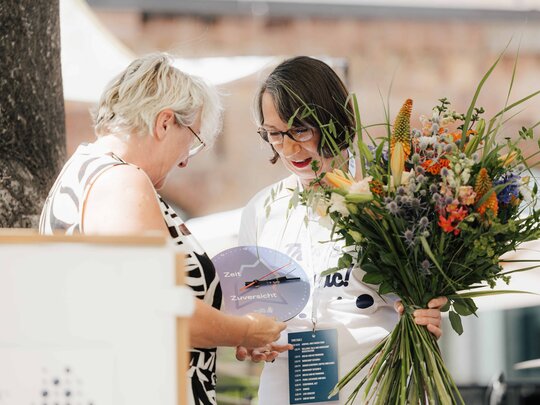 Theresia Bauer, Geschäftsführerin der Baden-Württemberg Stiftung und Wissenschaftsministerin a.D., überreicht Henrike Schön, Leiterin des Akademischen Auslandsamtes der Pädagogischen Hochschule Heidelberg, einen Blumenstrauß sowie eine Uhr.