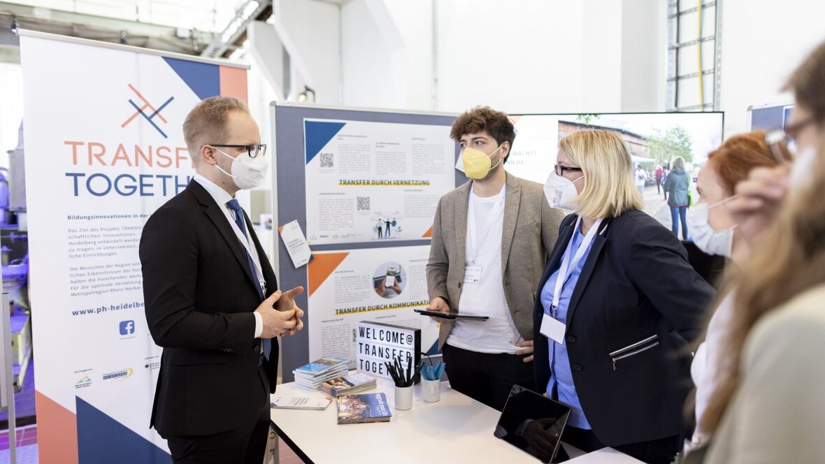Zu sehen ist das Team von Transfer Together bei einem Kongress im Gespräch mit Staatssekretär Dr. Jens Brandenburg.