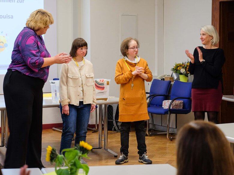 Louisa Kabbe und Susann Bensch sind auf der Feier anlässlich ihrer abgeschlossenn Qualifizierung. Rechts und links stehen die Leiterinnen des AW-ZIB, Prof. Karin Terfloth und Prof. Vera Heyl, und applaudieren.