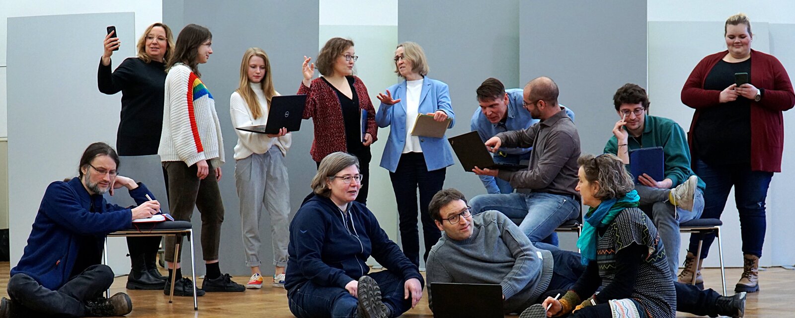 Mitlglieder des HGM Steuerkreises stellen das Bild "Die Schule von Athen nach". Manche stehen und sind im Gesrpäch, andere Personen sitzen oder liegen. Das Bild zeigt Austausch und Diskussion von PHeelgood der Pädagogischen Hochschule Heidelberg.